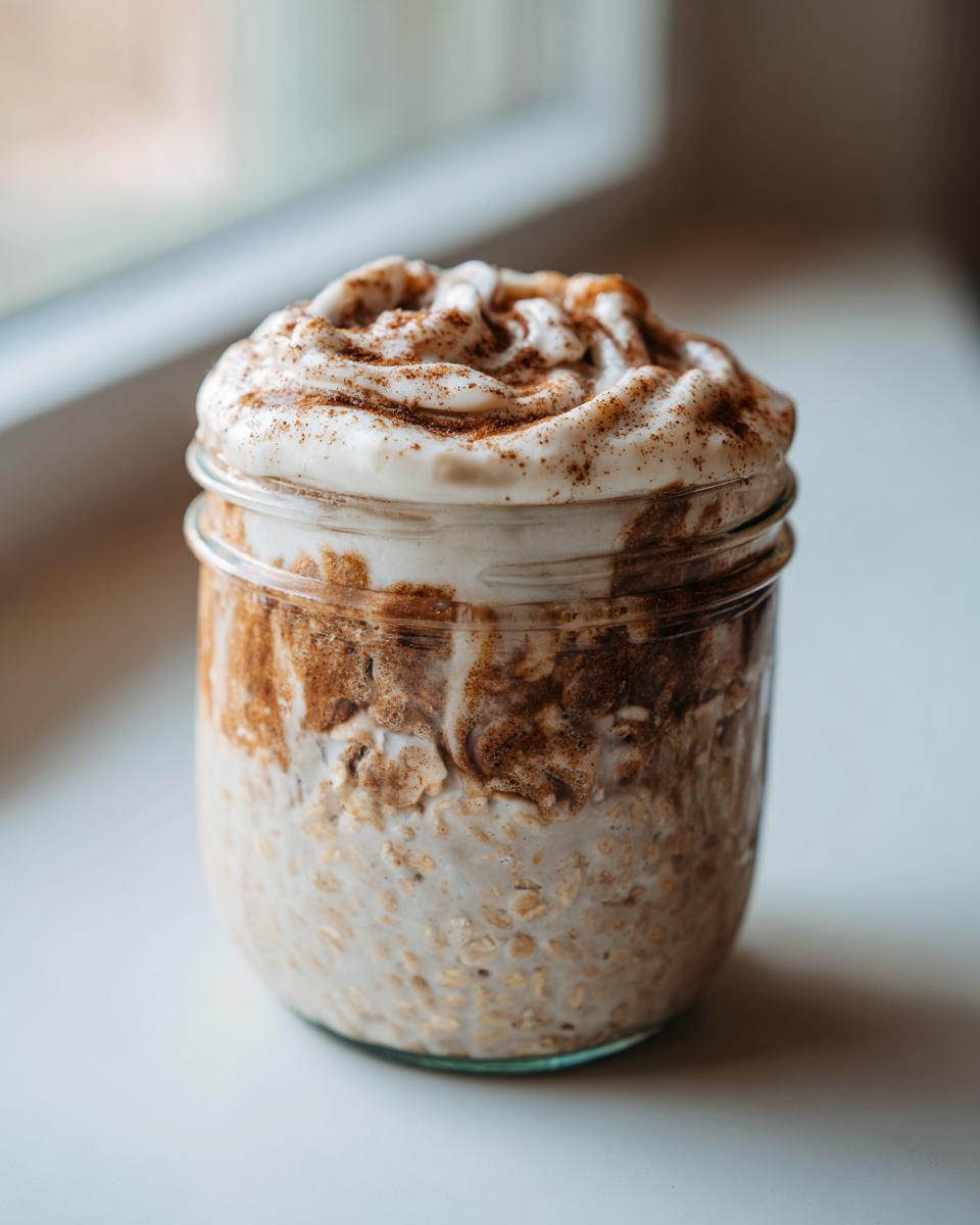 A glass jar filled with creamy cinnamon roll overnight oats, topped with a swirl of white frosting dusted with cinnamon.