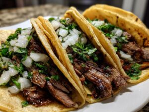 Close-up of three delicious Carne Asada Tacos filled with grilled steak, topped with diced white onion and fresh cilantro.