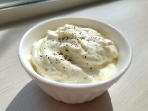 A small white bowl filled with thick, creamy alfredo sauce, topped with freshly cracked black pepper.