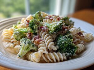 A close-up of creamy Broccoli Pasta Salad featuring fusilli pasta, bright green broccoli florets, and bacon bits served on a white plate.
