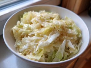 A close-up of a white bowl filled with tender, cooked cabbage coated in a creamy sauce, representing Cabbage Alfredo.