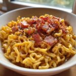 Close-up of creamy Carbonara Buldak Ramen noodles topped with crispy bacon bits and black pepper.