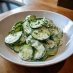 Close-up of a creamy cucumber salad with fresh dill dressing served in a white bowl.