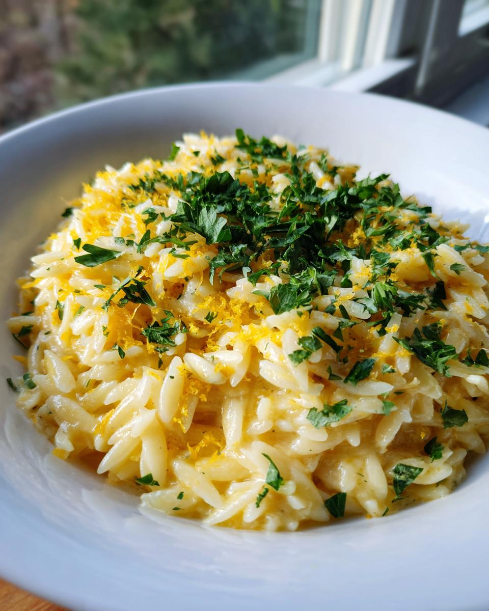 Close-up of creamy orzo pasta dish garnished heavily with bright lemon zest and fresh chopped parsley.