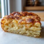 A close-up slice of creamy parmesan oven-baked potatoes showing layered, tender potatoes and a golden-brown, cheesy crust.