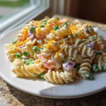 A serving of creamy Ranch Pasta Salad featuring rotini pasta, green peas, shredded cheddar, and red onion.