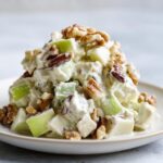 Close-up of a mound of creamy Waldorf Salad featuring diced green apples and topped generously with whole walnuts.