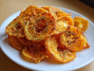 A close-up of a pile of golden, crispy baked onion ring chips seasoned with herbs, served on a white plate.