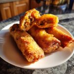 Close-up of crispy, golden brown homemade egg rolls stacked on a white plate, one cut open showing the savory filling.