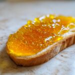 Close-up of a slice of toasted bread generously spread with bright orange Dandelion Jelly for Spring Toasts.