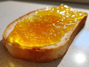 Close-up of bright yellow Dandelion Jelly spread thickly on a slice of toasted bread.