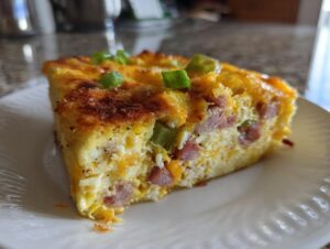 Close-up of a thick slice of Denver omelet bake showing eggs, ham, cheese, and green peppers, topped with scallions.