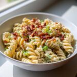 A close-up of creamy dill pickle bacon pasta salad made with rotini pasta, topped with crispy bacon bits.