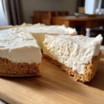 A close-up of a slice of creamy easy no bake cheesecake with a thick graham cracker crust on a wooden board.