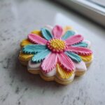 A beautifully decorated flower sugar cookie with vibrant pink, blue, and yellow piped icing petals.