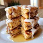 A tall stack of fluffy apple fritter pancakes cut open, drizzled heavily with white icing glaze and syrup.