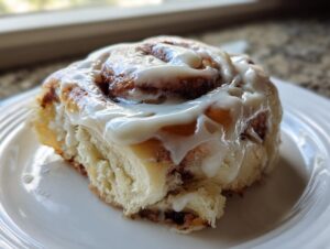 Close-up of a single, soft cinnamon sugar rolls topped with thick white icing, resting on a white plate.