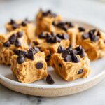 Several squares of frozen greek yogurt peanut butter bites topped with mini chocolate chips on a light plate.