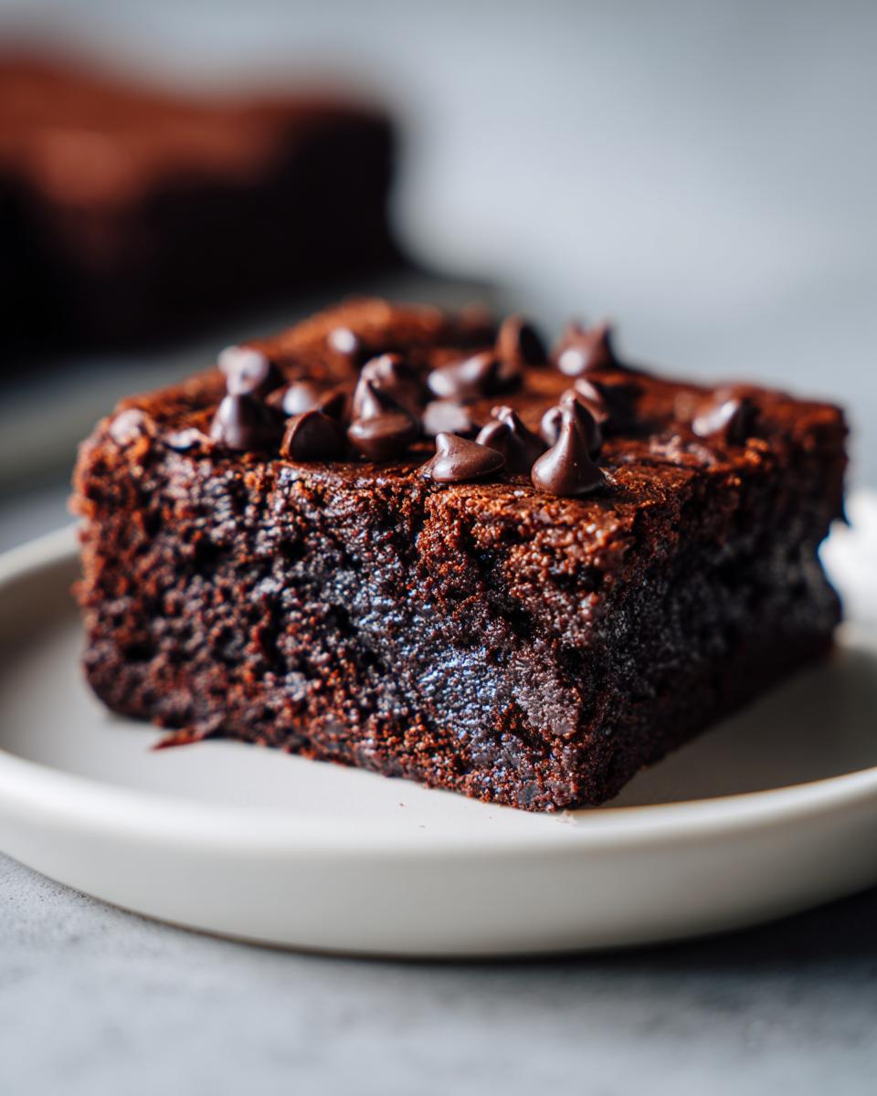 Close-up of a fudgy square of date brownies topped with melted chocolate chips on a light plate.