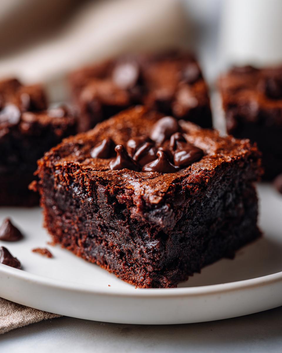 Close-up of a fudgy square of date brownies topped with melted chocolate chips on a white plate.