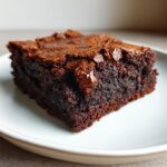 Close-up of a rich, fudgy slice of date brownies with visible chocolate chips on a white plate.