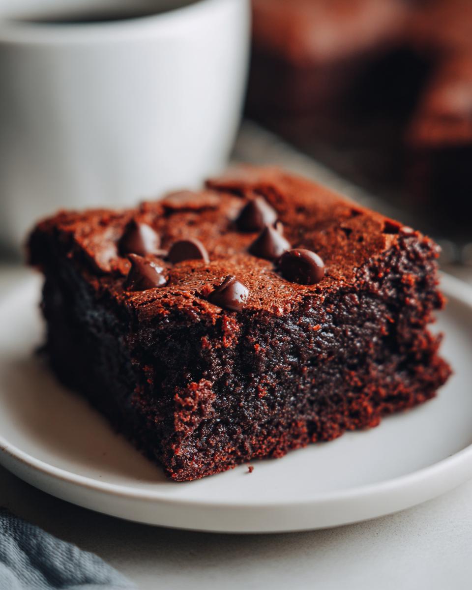 Close-up of a fudgy slice of date brownies topped with chocolate chips, next to a white mug.