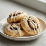 Close-up of three delicious cinnamon roll cookies drizzled with white icing on a small plate.