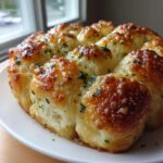 A close-up of freshly baked, pull-apart garlic cheese rolls with a golden, cheesy crust and parsley garnish.