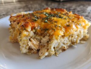 A close-up serving of cheesy green chile chicken and rice casserole topped with melted cheddar and parsley.