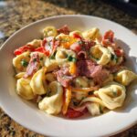 A white bowl filled with creamy Grinder Tortellini Salad featuring tortellini, cured meats, and bell peppers.