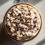 Overhead view of creamy high protein cookie dough overnight oats topped generously with mini chocolate chips in a glass jar.