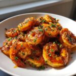A close-up of glossy, glazed hot honey shrimp recipe piled high in a white bowl, garnished with fresh parsley.