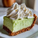 A close-up of a rich slice of key lime pie recipe with a graham cracker crust and topped with swirls of whipped cream.
