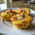 Three baked cups made from Leftover Spaghetti Carbonara, topped with melted cheese and bacon bits.