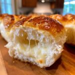 Close-up of a mini grilled cheese hawaiian roll pulled apart showing melted, stringy cheese inside soft white bread.