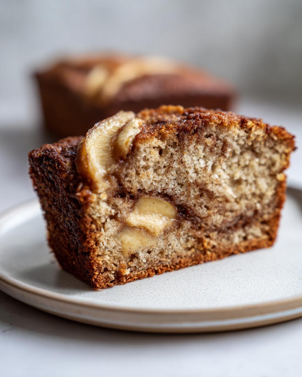 Close-up of a moist slice of apple bread showing chunks of cooked apple and a cinnamon swirl.