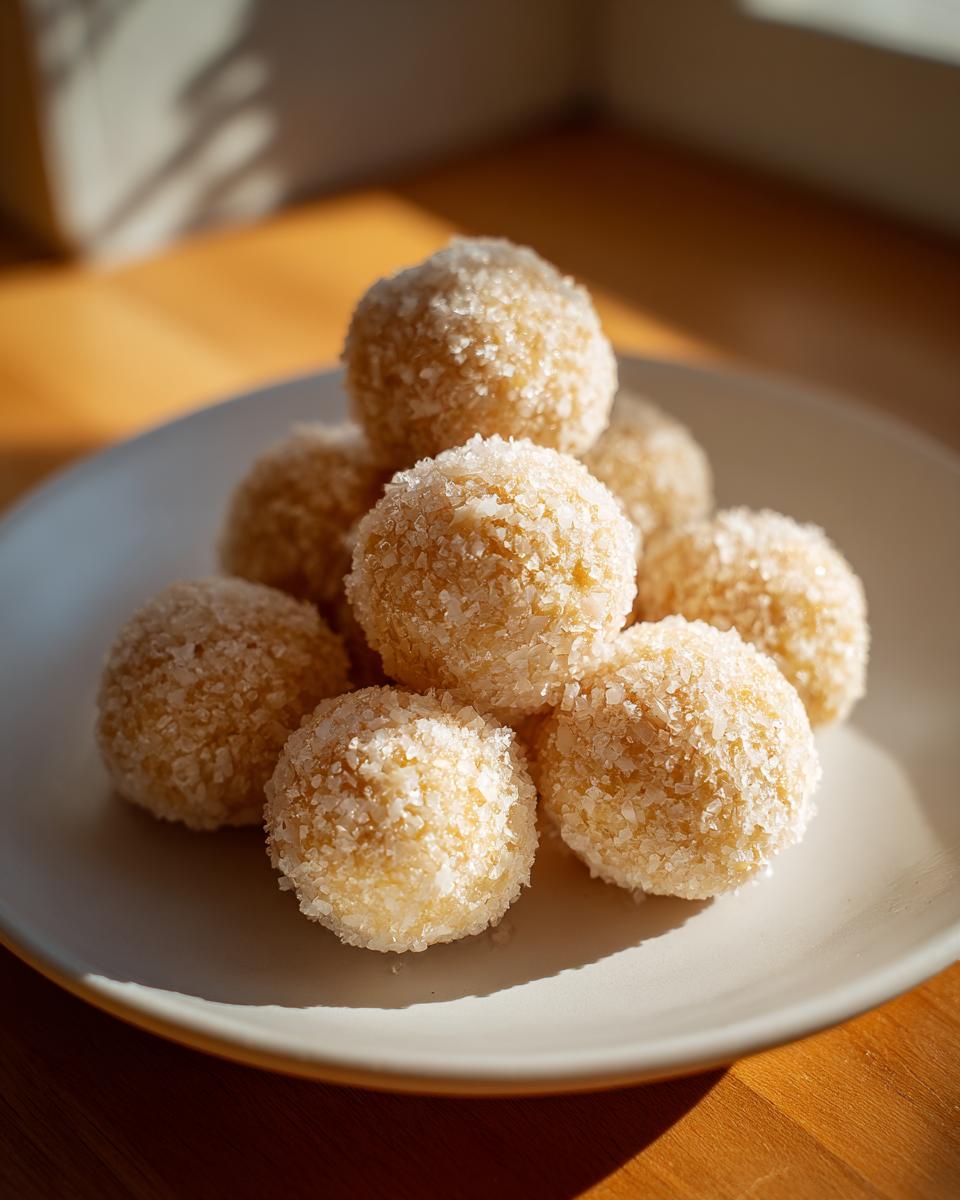 A close-up of several no-bake margarita balls stacked on a white plate, heavily coated in shredded coconut.