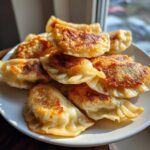 A pile of perfectly pan-fried Cabbage Dumplings with golden-brown, crispy bottoms served on a white plate.