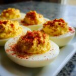 Close-up of creamy paula deen deviled eggs topped generously with bright red paprika.