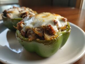 Two baked green bell peppers filled with steak, onions, and topped with melted white cheese, ready to eat as philly cheesesteak stuffed peppers.