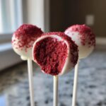 Close-up of three red velvet cake pops dipped in white chocolate, one bitten to show the rich red interior.