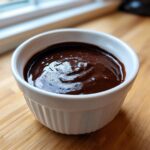 Close-up of smooth, glossy chocolate fondue served in a small white fluted ramekin.