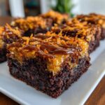 A close-up of a rich, fudgy square of samoa brownies topped with caramel, toasted coconut, and chocolate drizzle.