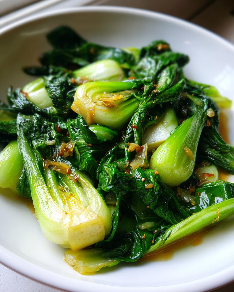 Close-up of vibrant green Sautéed Bok Choy glistening with sauce and garlic served in a white bowl.