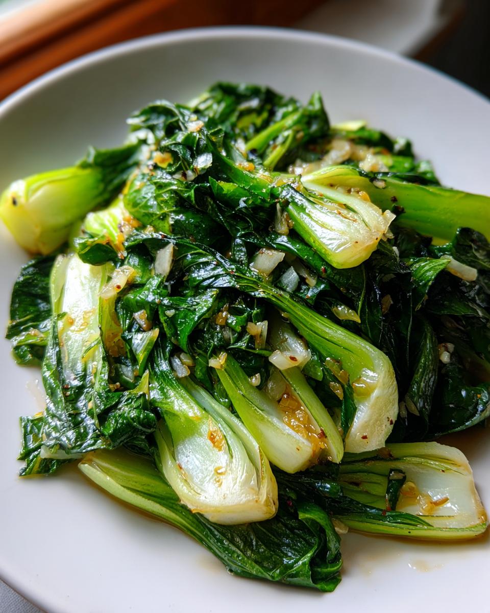 A close-up serving of vibrant green Sautéed Bok Choy mixed with garlic and sauce on a white plate.
