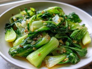 A close-up of vibrant green Sautéed Bok Choy glistening with sauce and garlic pieces in a white serving bowl.