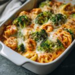Close-up of a bubbly, cheesy sheet pan broccoli tortellini bake in a white casserole dish.