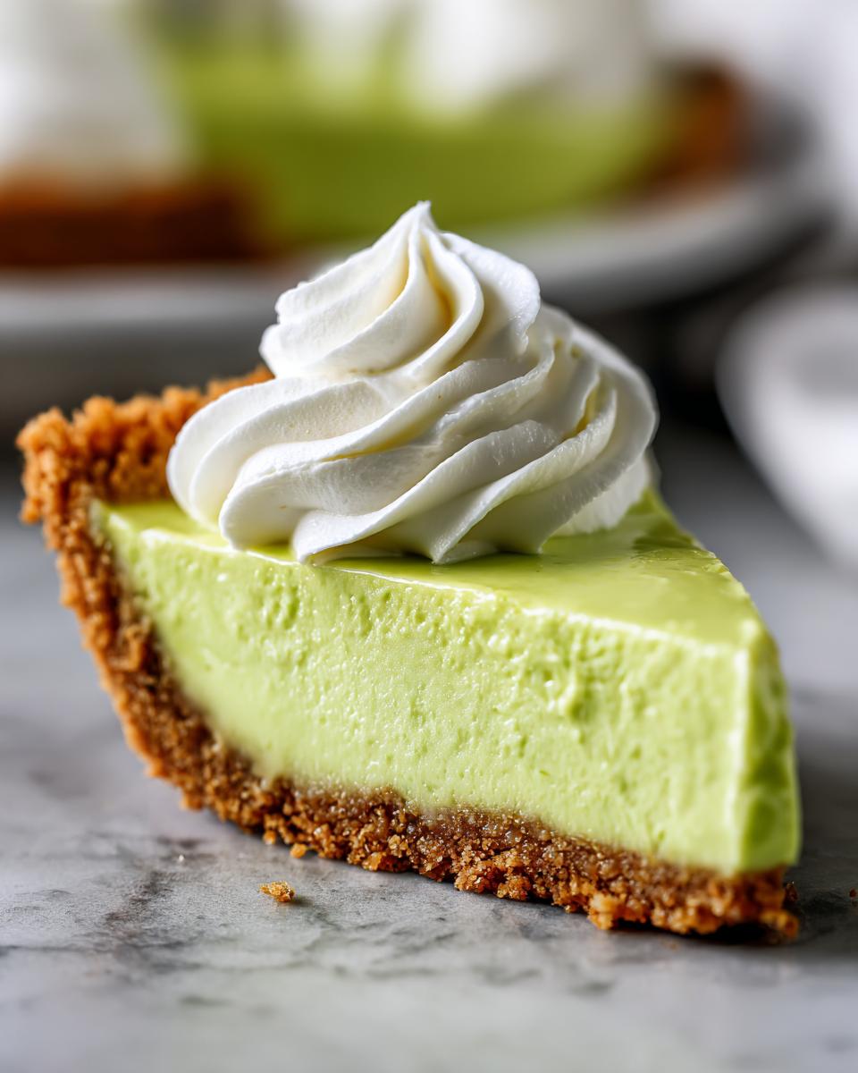 A close-up of a perfect slice of key lime pie recipe with a graham cracker crust and a swirl of whipped cream.