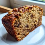 Close-up of a moist slice of sugar free banana bread topped with walnuts on a white plate.