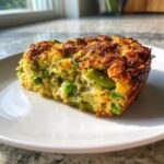 A close-up slice of a golden-brown Spring Vegetable Casserole featuring bright green peas and asparagus pieces.